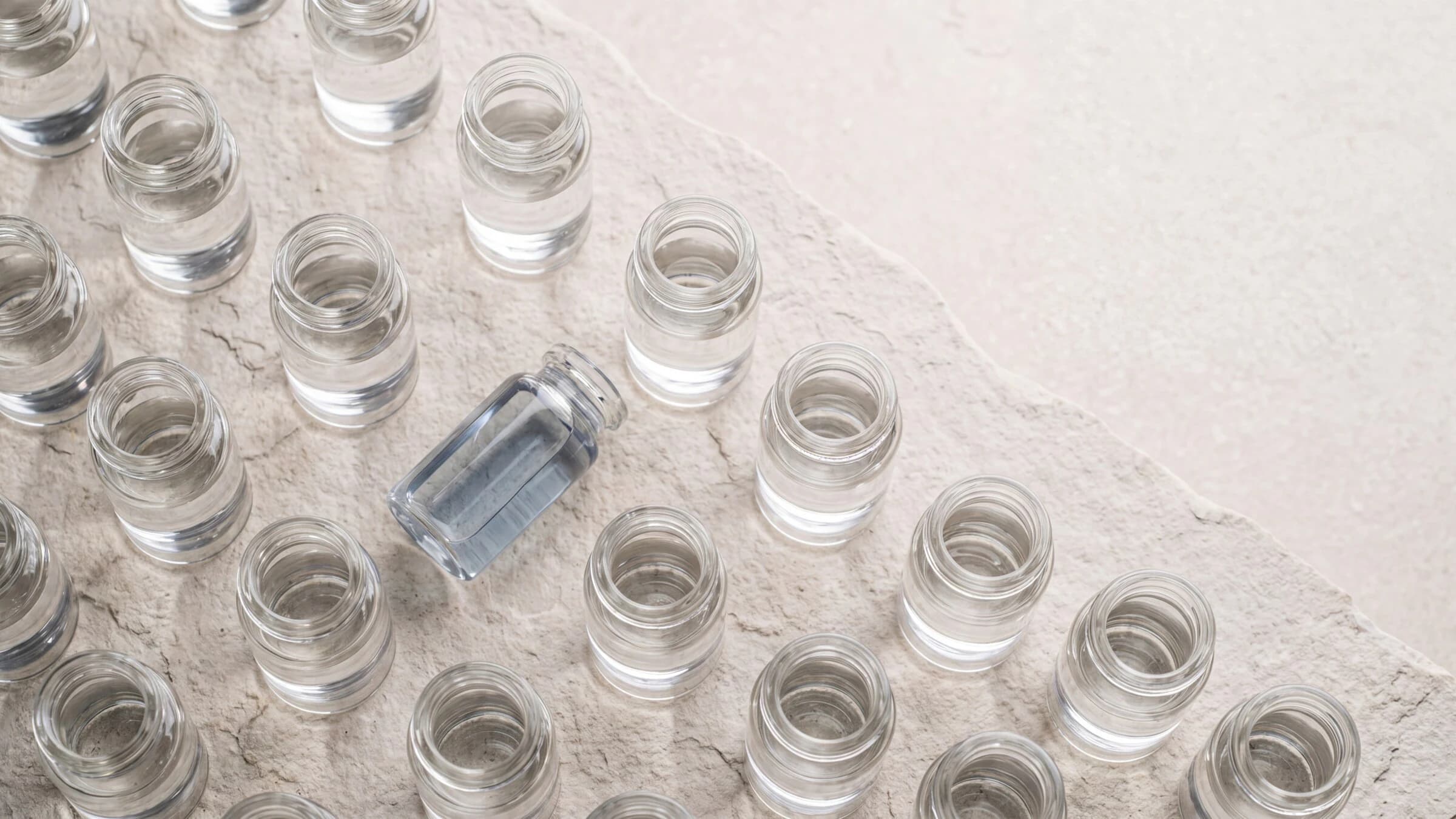 Clear laboratory water-sample vials arranged across pale stone, with one vial tilted at the center