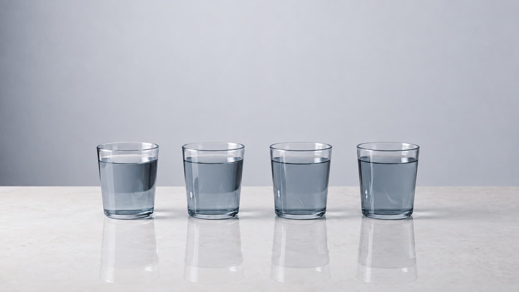 Four matching glasses of clear water arranged on pale stone in soft natural light