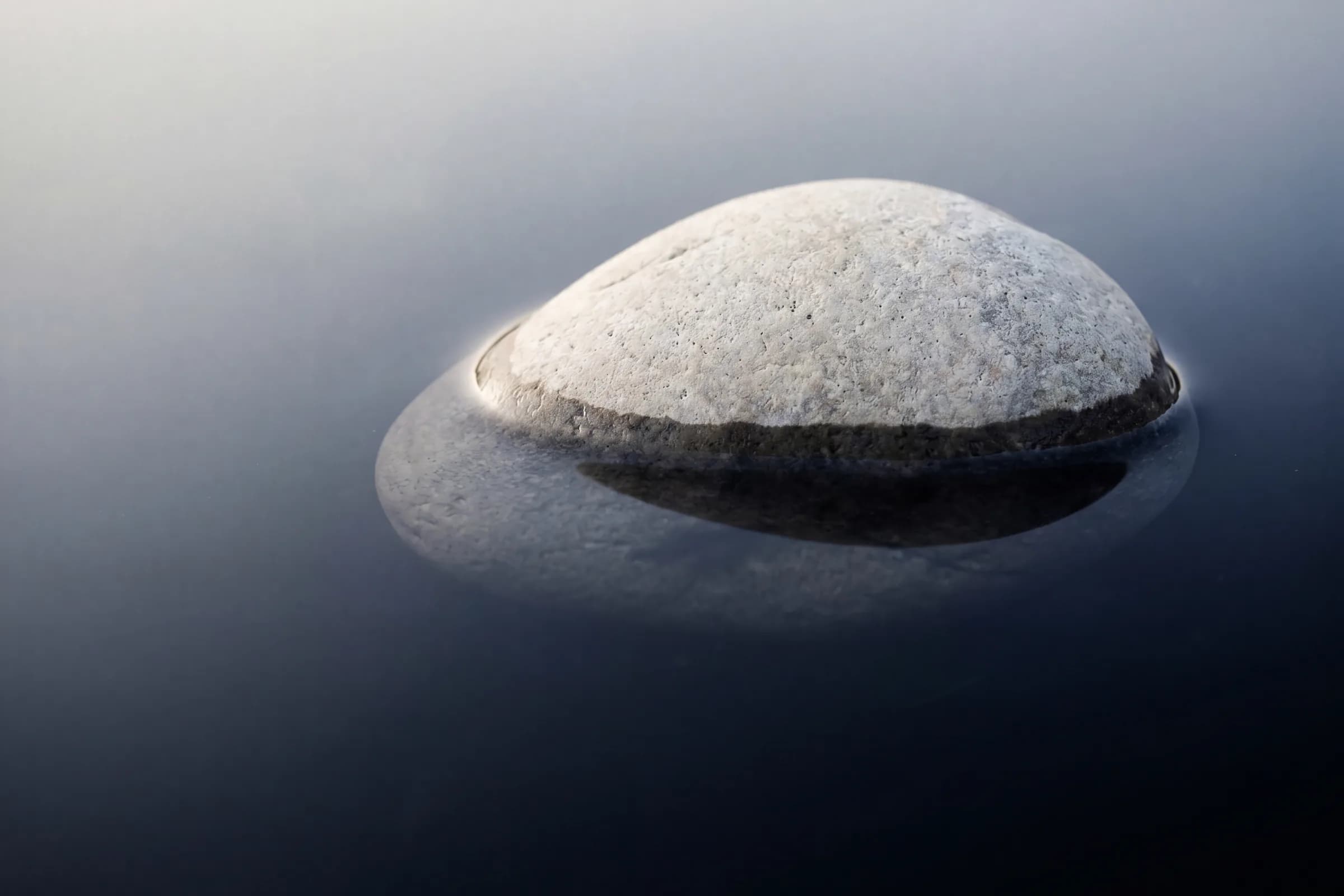 A smooth dome-shaped stone half-submerged in still dark water, the waterline splitting it